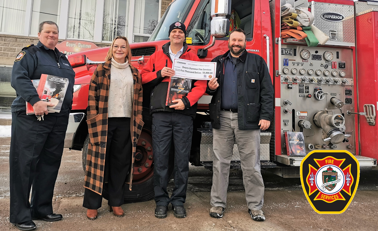 Deputy Fire Chief Huffman, Mayor Watson, Chief Pedersen and Ian Moase stand in front of a fire truck holding firefighting textbooks and an oversized cheque. 